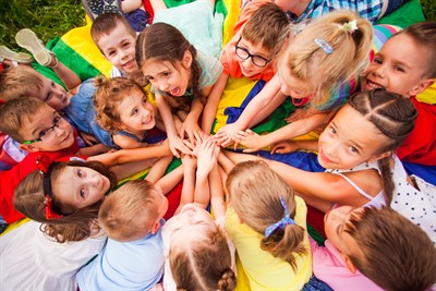 Children in a circle holding hands and laying on a parachute