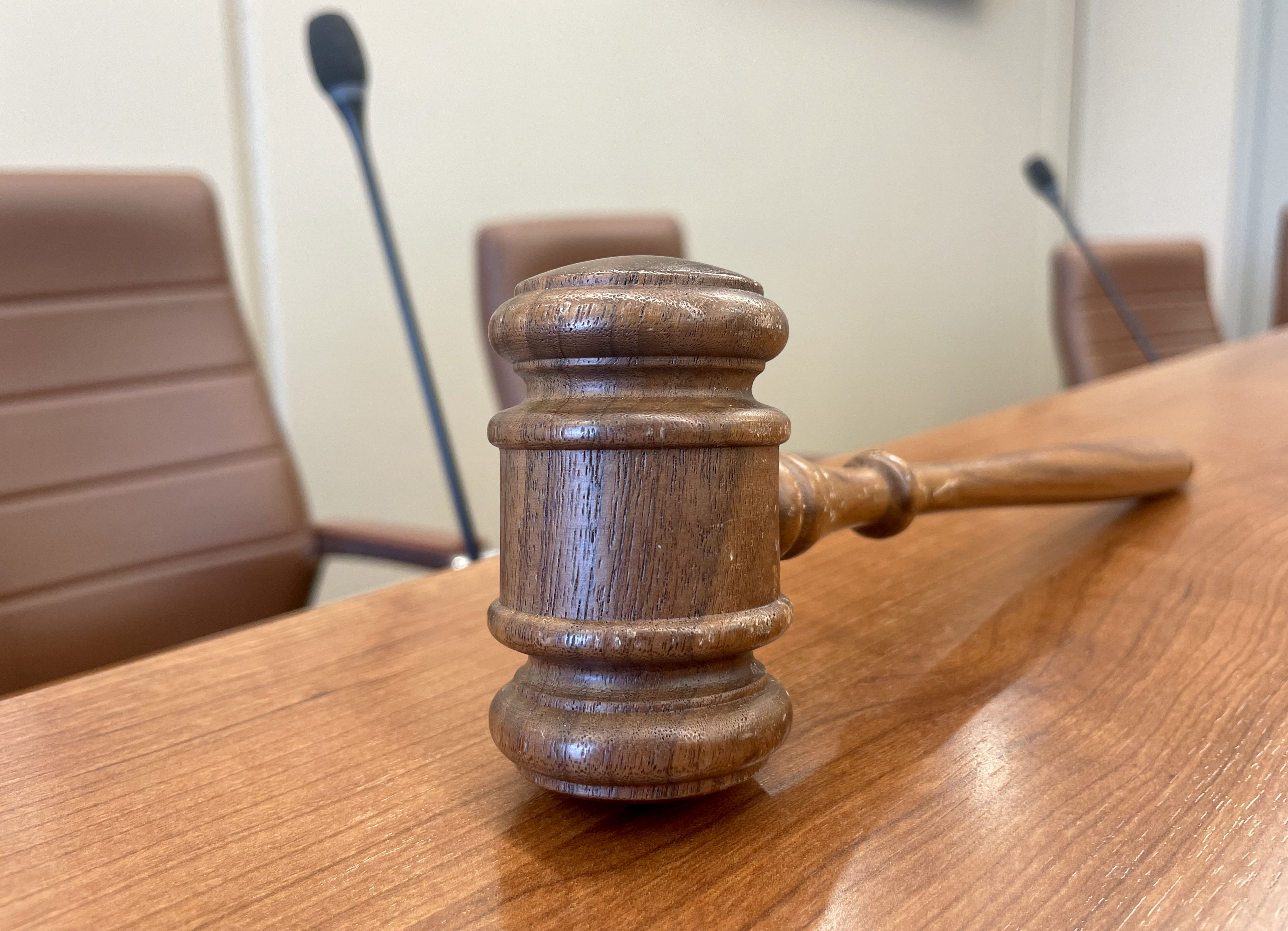 Gavel on a table with chairs in the background.
